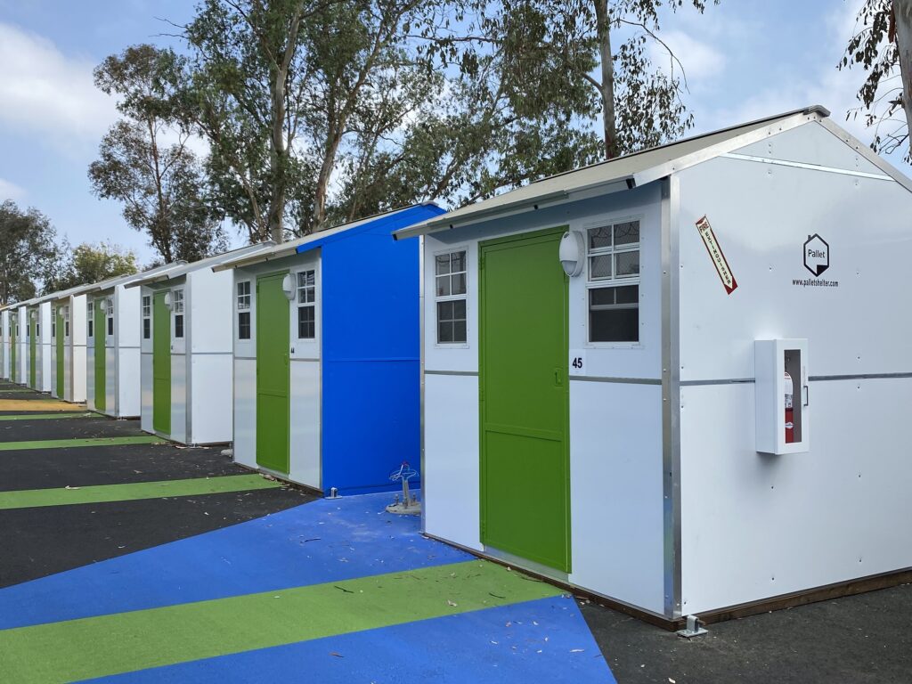 Row of white Pallet shelters with green doors in a village.