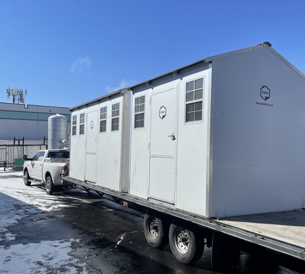 Two fully assembled Pallet shelters arriving at a testing facility on top of a flat bed attached to a truck.