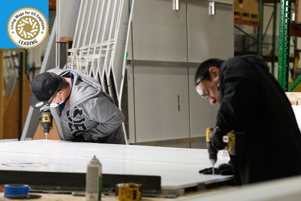 Two Pallet employees build shelters. In the top left the corner of the photo is the Living Wage for US certification seal.