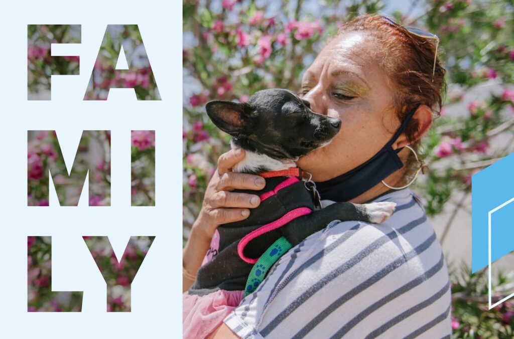 A woman wearing a striped shirt kisses a small black dog, which is being held in her arms.