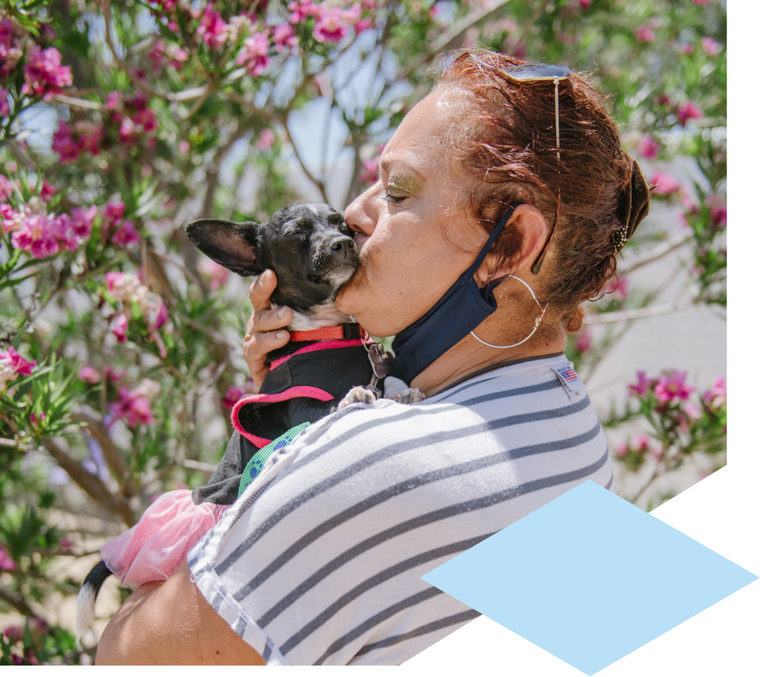 A woman in a striped t-shirt kisses a small chihuahua in her arms.