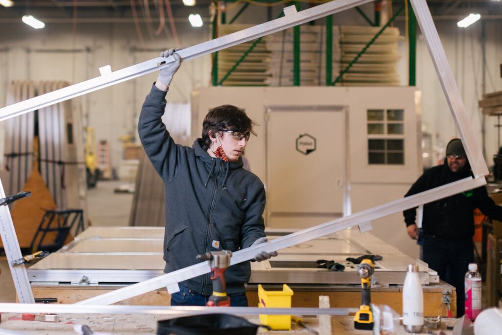 A Pallet manufacturing specialist holds up an aluminum door frame for a shelter in the factory.