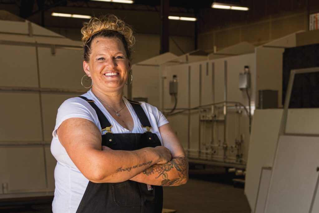 Lacey shown from the waist up standing next to Pallet bathrooms that are being constructed.